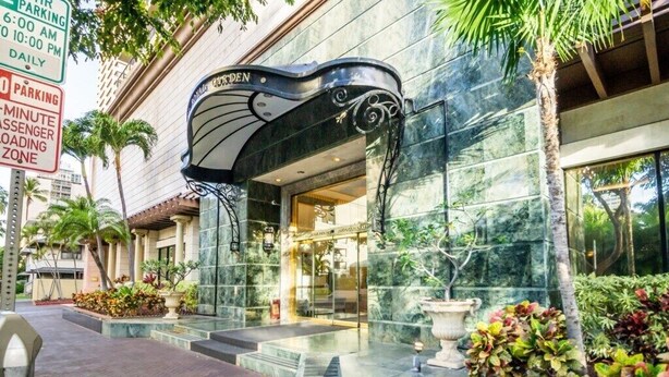 A hotel entrance with a modern design, a parking sign, and a well-maintained outdoor area with plants.