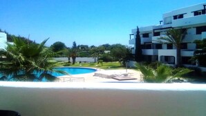 A pool area with a clear blue pool, surrounded by palm trees and a white building with balconies. - Apartment with pool view at La Cassia 4187 complex (Cabo Negro)