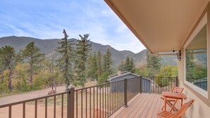 Eine Holzterrasse mit Metallgeländer, mit Blick auf eine Berglandschaft mit Bäumen und einem kleinen Gebäude.