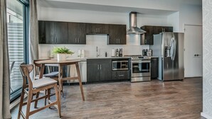Eine moderne Küche mit dunklen Schränken, Edelstahlgeräten und einem Holztisch.