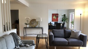 A living room with a grey sofa, a dark grey couch, a small table, a large wall clock, and a lamp. - Beautiful Marina Home - 2Bed 2Bath - 1 block from Marina Blvd! (San Francisco)