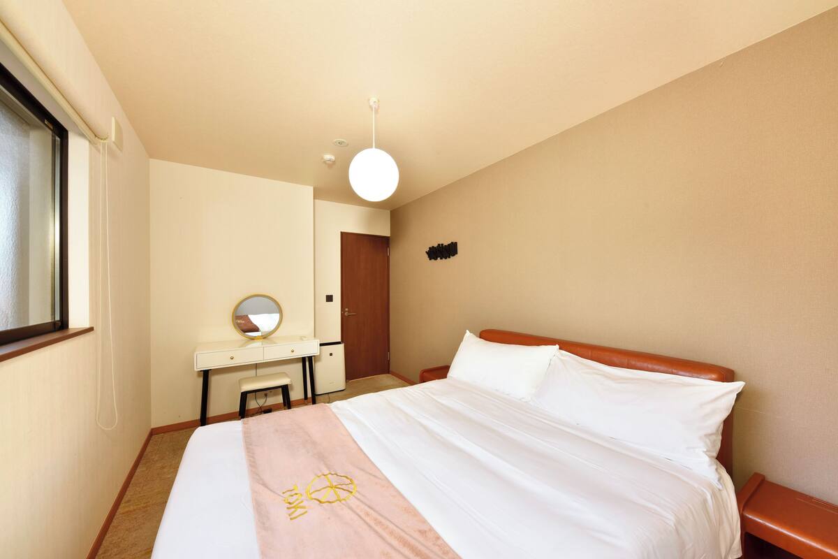 A hotel room with a bed, a desk, a chair, a mirror, and a door.