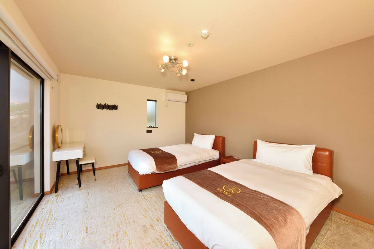 A hotel room with two beds, a desk, and a sliding glass door.
