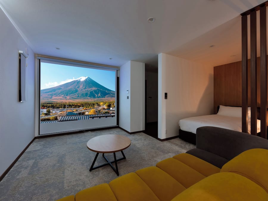 Quarto de hotel moderno com uma janela grande que oferece vista para uma montanha e para a paisagem urbana.