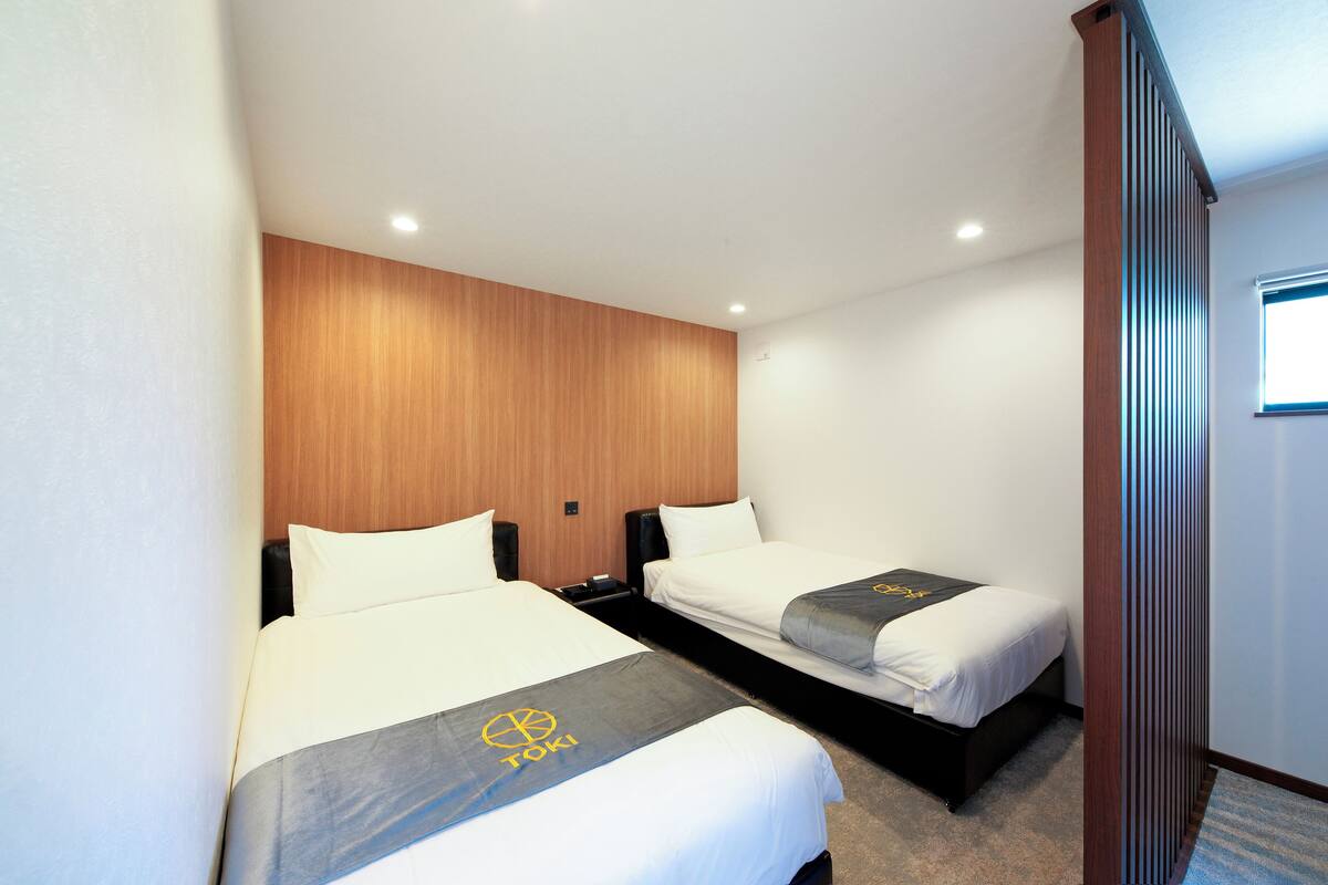 A hotel room with two beds, wooden headboard, white bedding, and a logo on the bedspread.