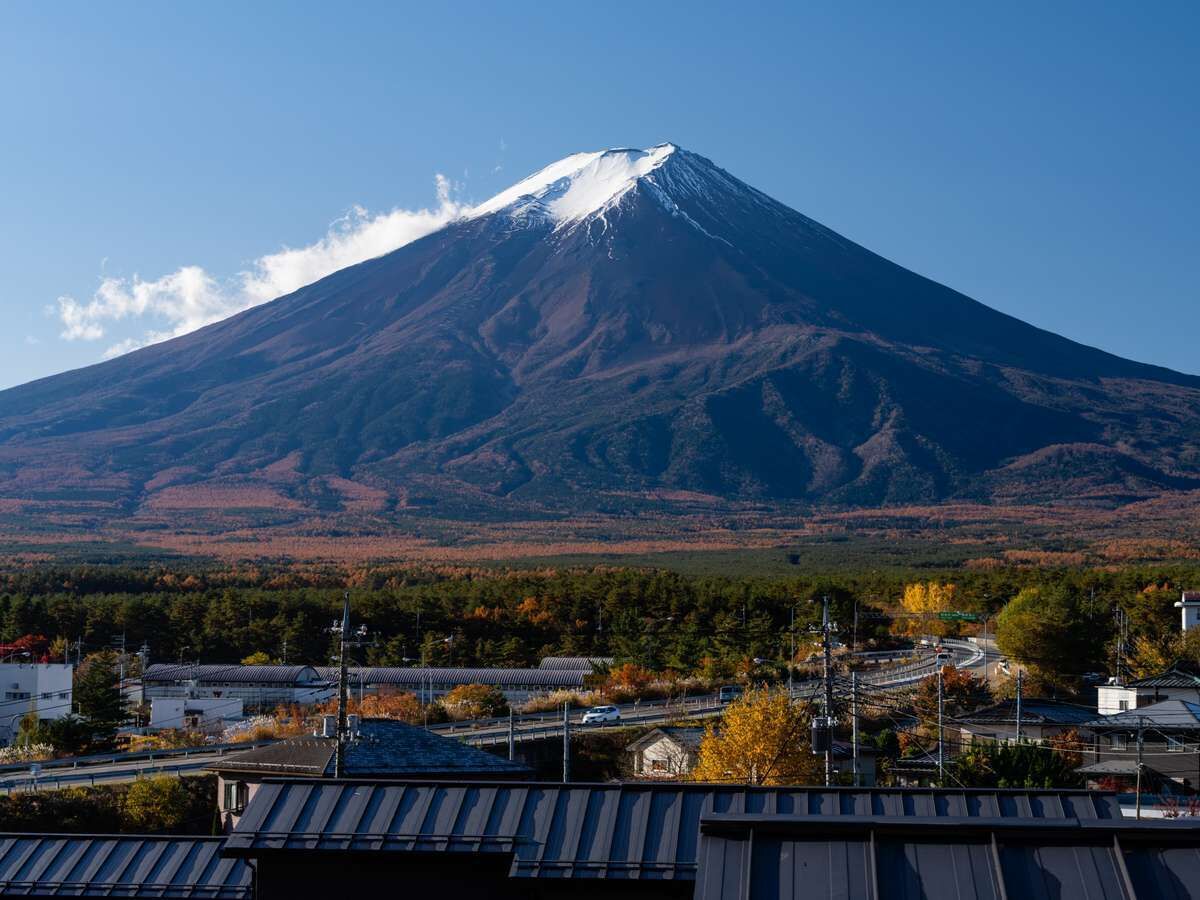 A mountain with a snow-capped peak, surrounded by autumn-colored trees and a town with buildings and roads in the foreground.