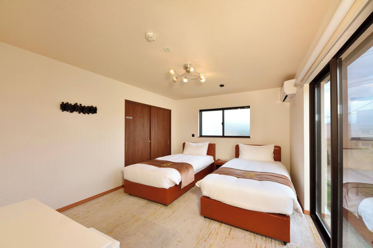 A hotel room with two beds, a wardrobe, a window, and a ceiling light fixture.