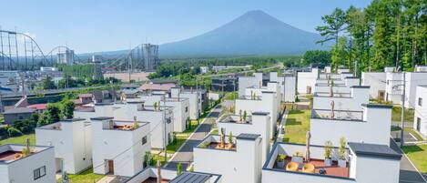 Zona residencial com casas modernas, vista para um vulcão e uma montanha-russa ao fundo.