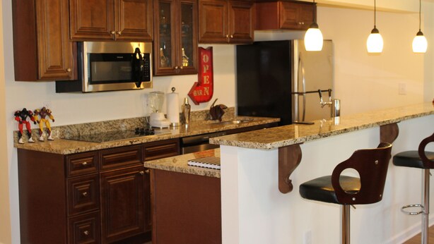 A kitchen with wooden cabinets, stainless steel appliances, granite countertops, and bar stools.
