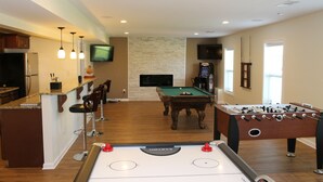 A modern kitchen with a bar area, a pool table, and a foosball table.