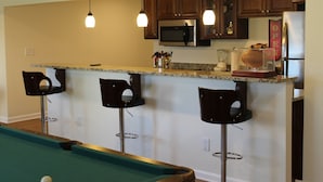 A kitchen with dark wooden cabinets, a microwave, a refrigerator, and a bar area with stools.