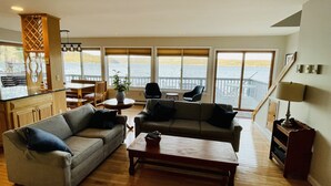 A spacious living room with a view of a lake, wooden flooring, and a large window. - Lakeside Life on Keuka's Water's Edge (Hammondsport)