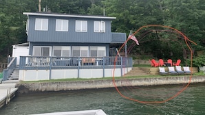 A two-story house with a dock, a flag, and red chairs by the water. - Lakeside Life on Keuka's Water's Edge (Hammondsport)