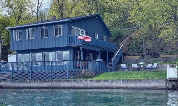 Ein blaues Haus mit einer amerikanischen Flagge, einem Balkon und einer Anlegestelle, die sich in ein Gewässer erstreckt.
