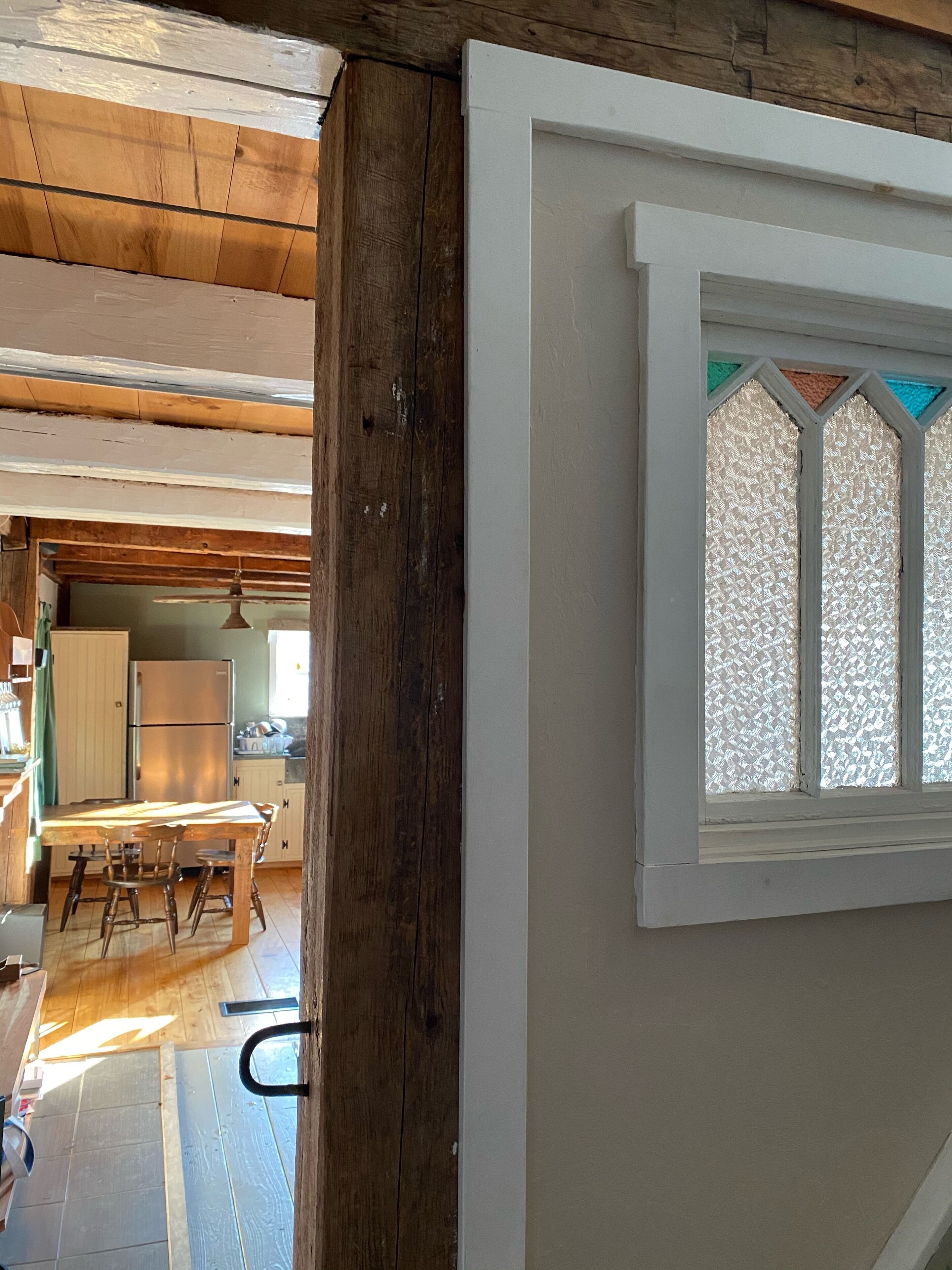 A rustic kitchen with wooden beams, a double-door refrigerator, and a window with patterned glass.