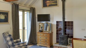 A cozy room with a bed, a chair, a dresser, a mirror, a fireplace, and a painting on the wall.