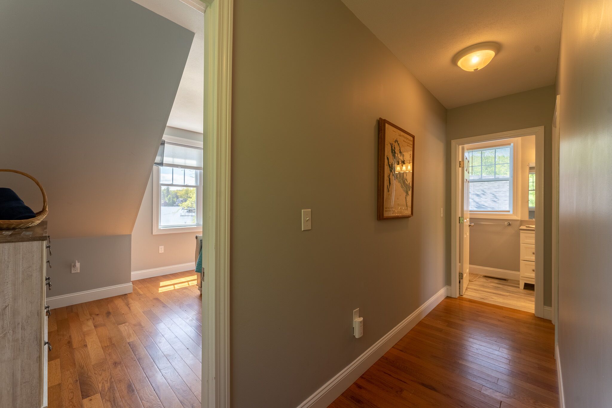 Un couloir avec un plancher en bois, un luminaire au plafond et une porte donnant accès à une salle de bain.