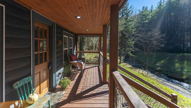 A wooden porch with a chair and a welcome mat, overlooking a forested area. - Hidden Cabin on Old Field Creek Quaint cottage near Boone with creek frontage (Fleetwood)