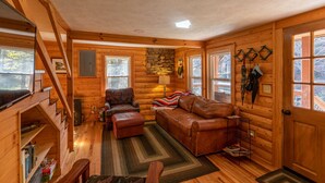 A cozy cabin interior with a wooden interior, a fireplace, a sofa, and a chair. - Hidden Cabin on Old Field Creek Quaint cottage near Boone with creek frontage (Fleetwood)