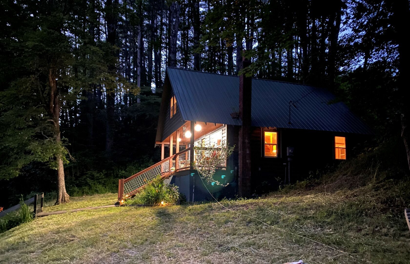 Une cabane avec un escalier en bois menant à une terrasse, le tout entouré d’arbres.