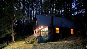 A cabin with a wooden staircase leading to a deck, surrounded by trees. - Hidden Cabin on Old Field Creek Quaint cottage near Boone with creek frontage (Fleetwood)