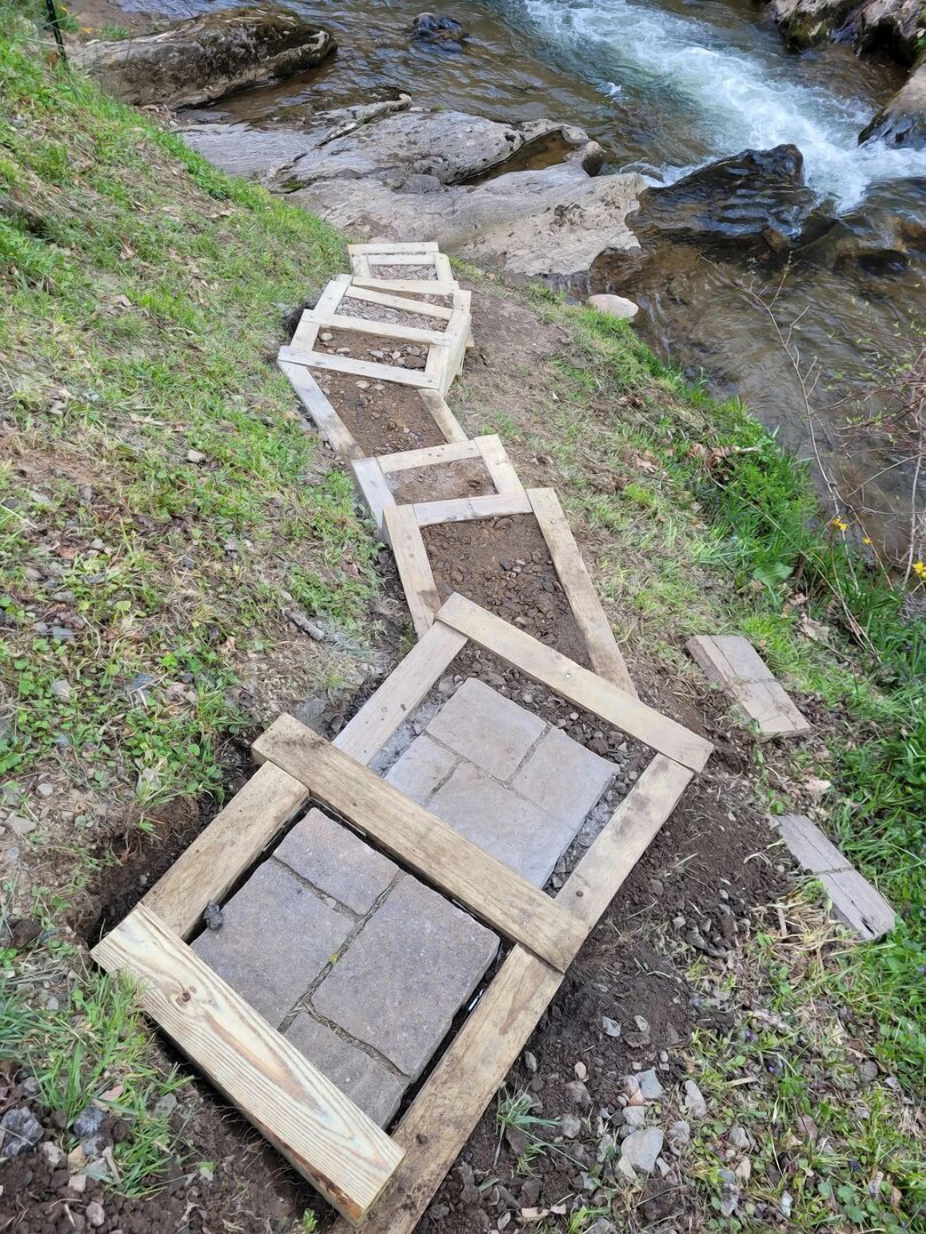 Un sentier en bois mène à une construction en pierre, au bord d’un ruisseau.