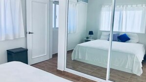 Un dormitorio con cama, mesita de noche, lámpara y ventana con cortinas.