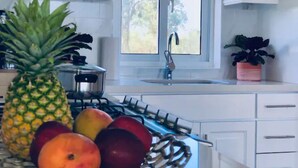 Una cocina con armarios blancos, estufa, lavaplatos y ventana con vista a árboles.