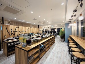 A modern cafe with a wooden counter, bar stools, and a variety of food items displayed. - Green Rich Hotel Miyazakitachibanadori 2 Artificial Hot Spring Futamata Yunohana (Miyazaki)