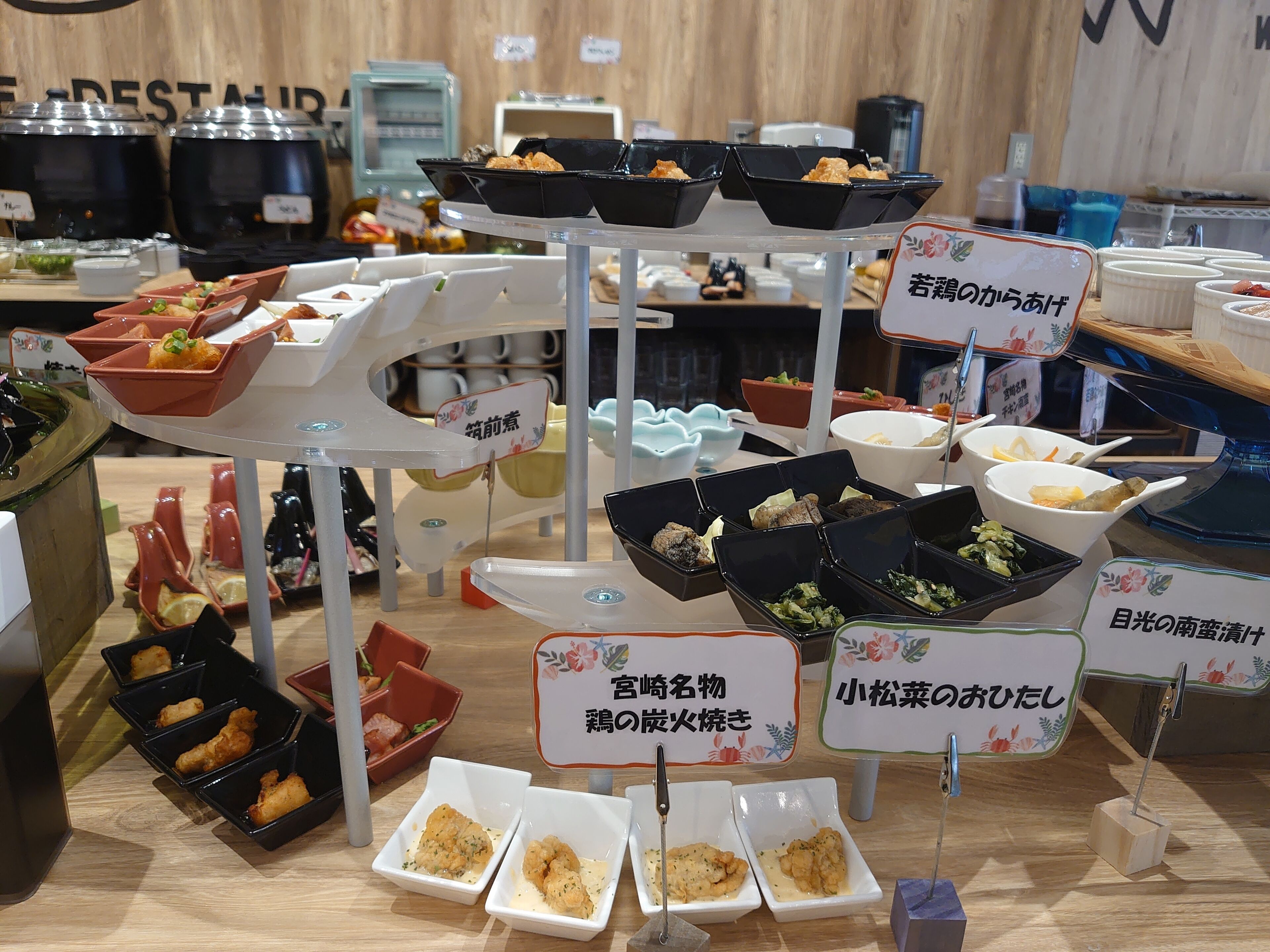 A buffet setup with various dishes in trays and bowls, some labeled in Japanese.