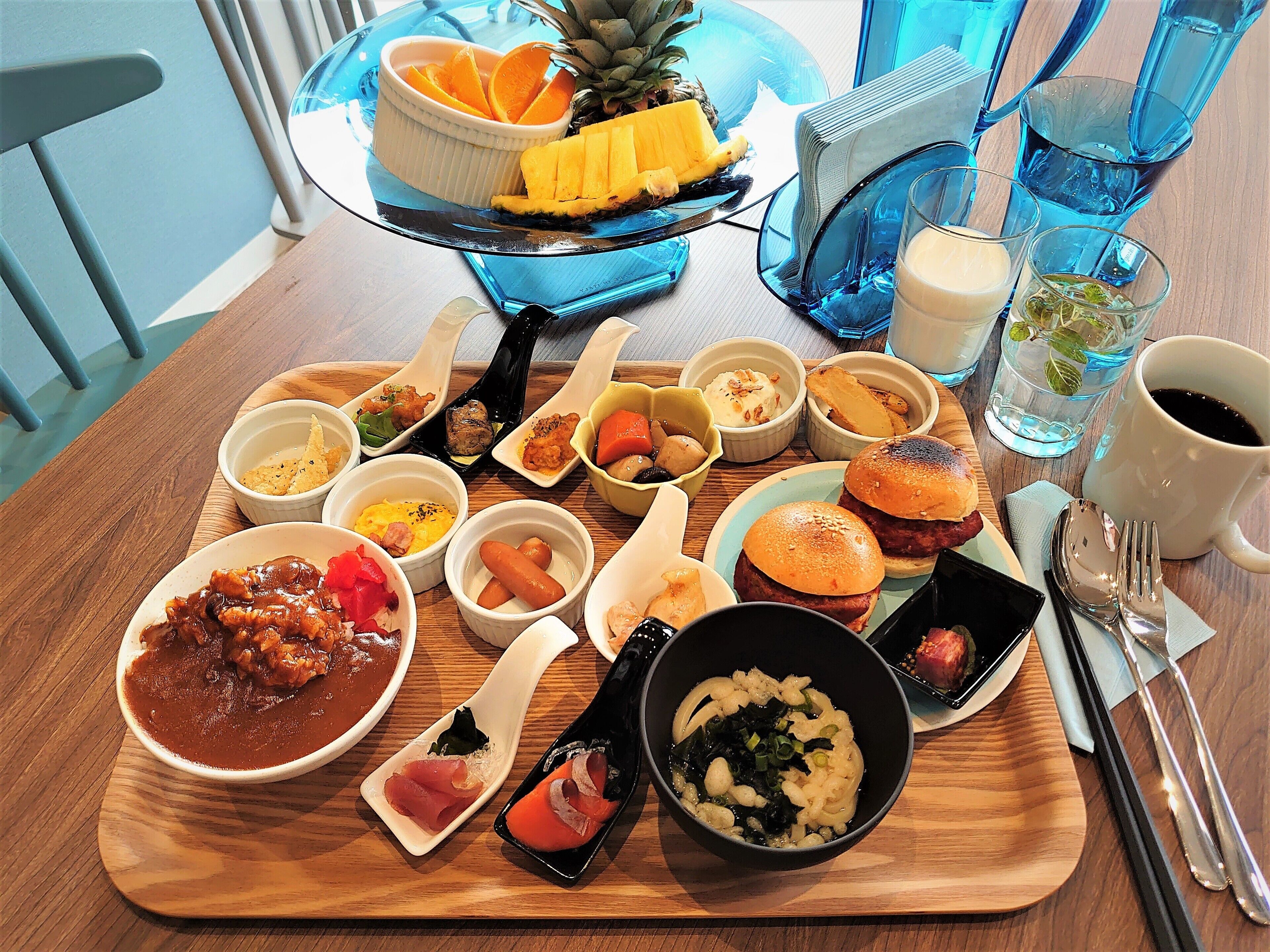A variety of dishes on a wooden table, including a bowl of soup, a plate of meat, and several small dishes with different foods.