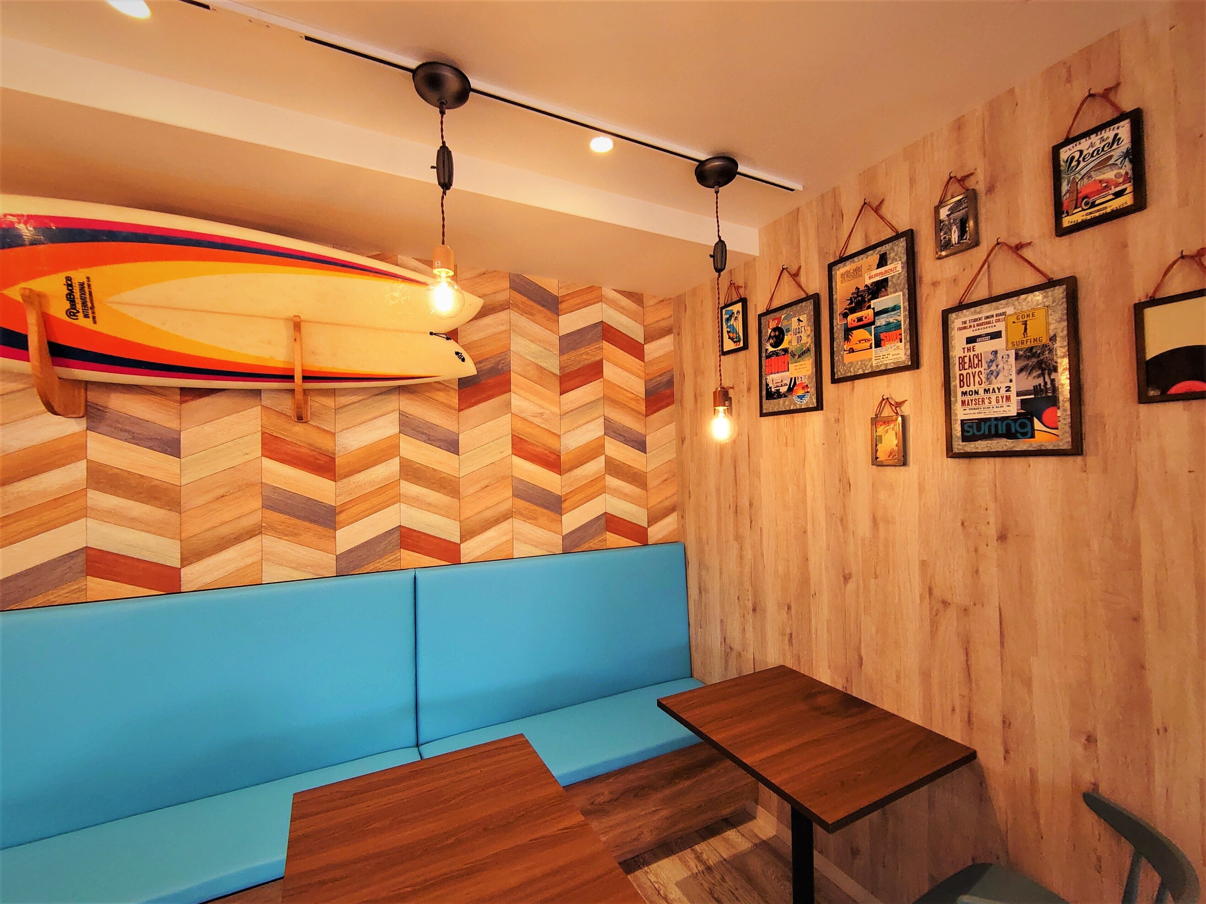 A restaurant interior with a wooden herringbone wall, blue seating, and a surfboard decoration.