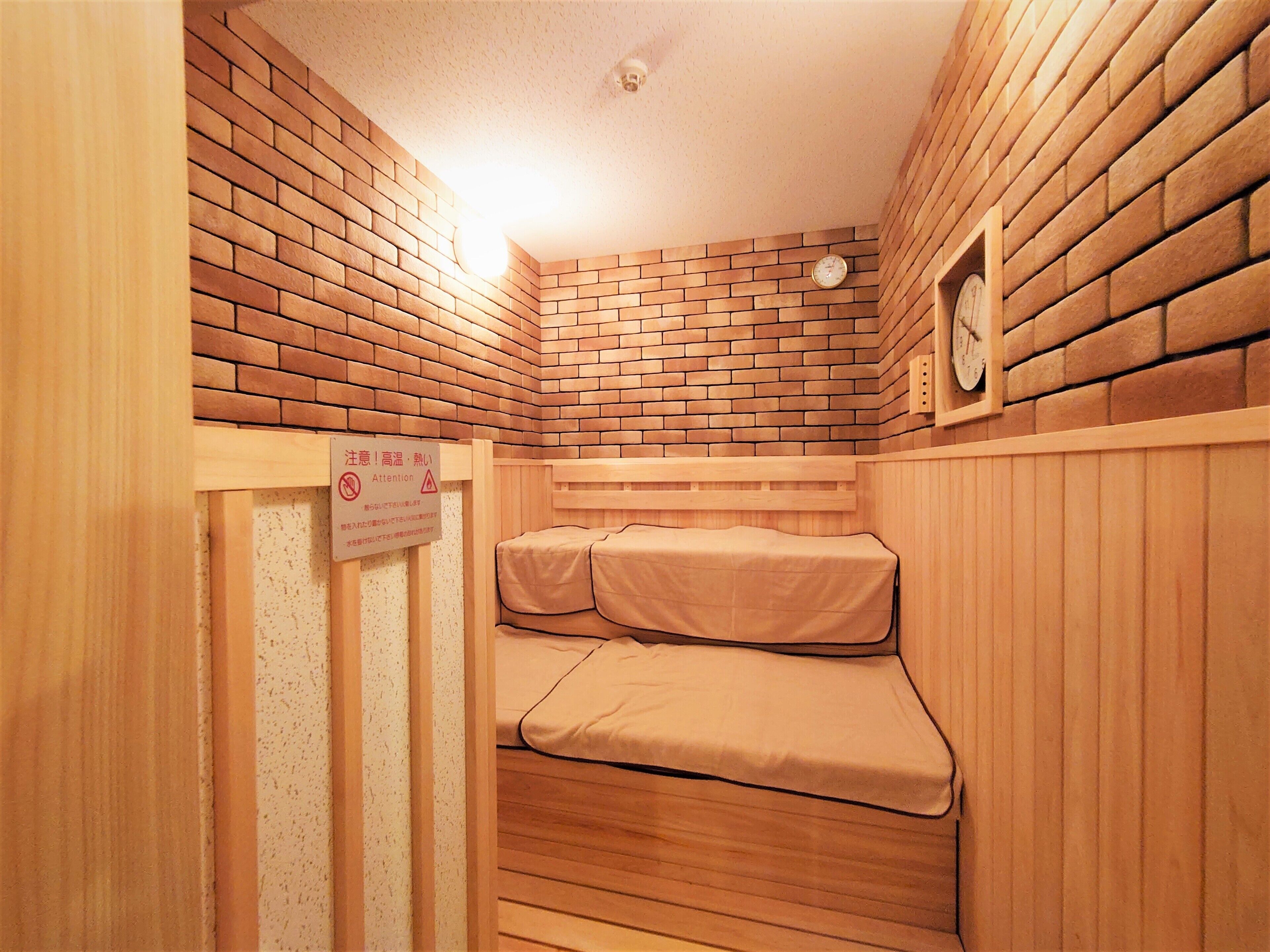 Ein kleiner, abgeschlossener Raum mit Backsteinwand, einer Holzbank und einem Bett mit Matratze.