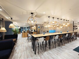 A modern restaurant with a long wooden table, multiple chairs, and geometric pendant lights.