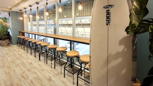 A bar area with wooden stools and a surfboard leaning against the wall. - Green Rich Hotel Miyazakitachibanadori 2 Artificial Hot Spring Futamata Yunohana (Miyazaki)