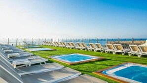 A rooftop pool area with multiple lounge chairs and a swimming pool, overlooking a beach and ocean. - Hotel Lopez - Suitehotel Playa del Ingles (San Bartolomé de Tirajana)