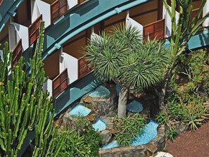 A hotel with a modern design, featuring a pool area surrounded by various plants and cacti.