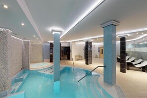 A swimming pool area with a tiled floor, a pool with a ladder, and lounge chairs.