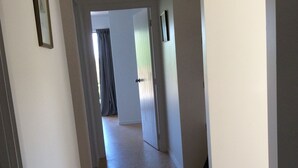 A hallway with a carpeted floor, white walls, and a door at the end. - House wth the Orange Door (Tasman)