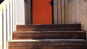 A wooden staircase leading to a door with a black frame and an orange door. - House wth the Orange Door (Tasman)