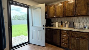 Une cuisine avec des meubles en bois, un pare-feu en carrelage et une porte donnant sur un patio.