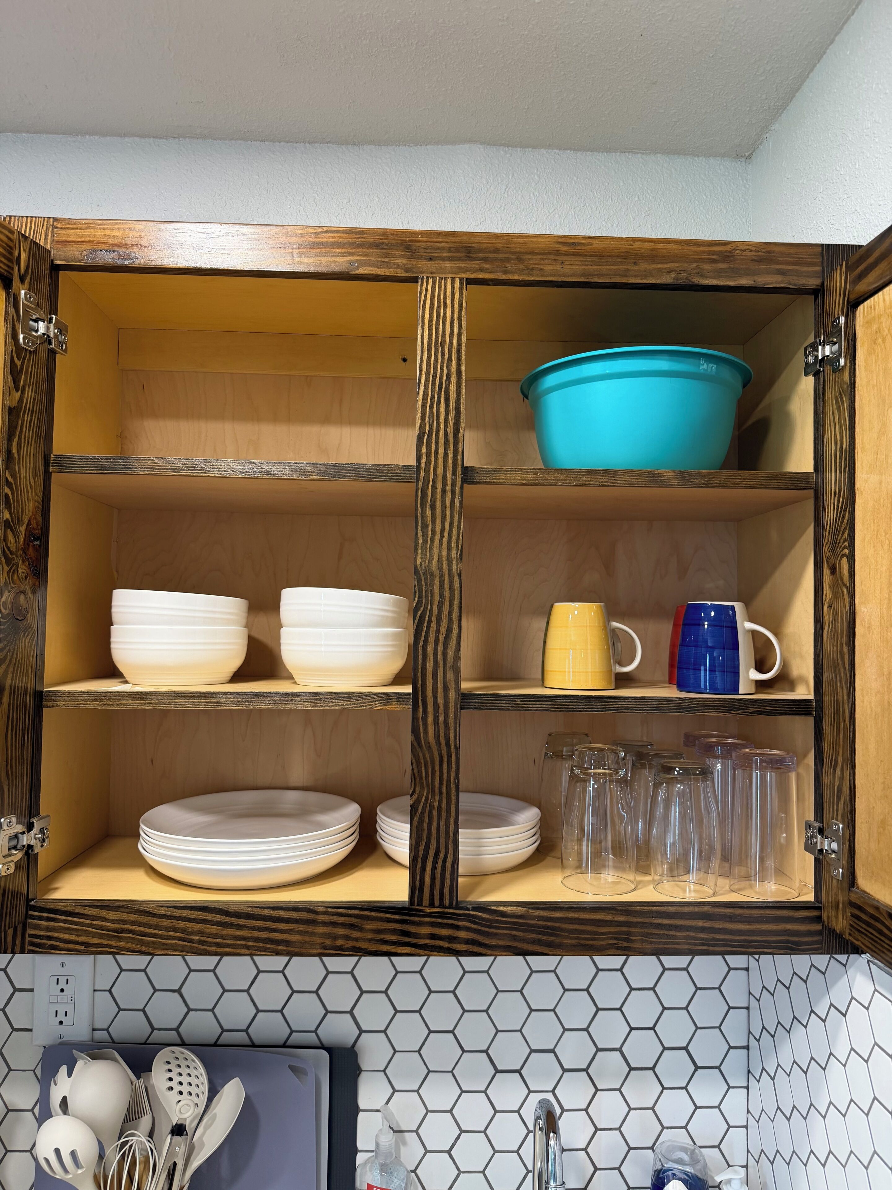 Een keuken met houten kastjes, een blauwe kom, witte borden, een gele mok en een backsplash van honingraatmozaïek.