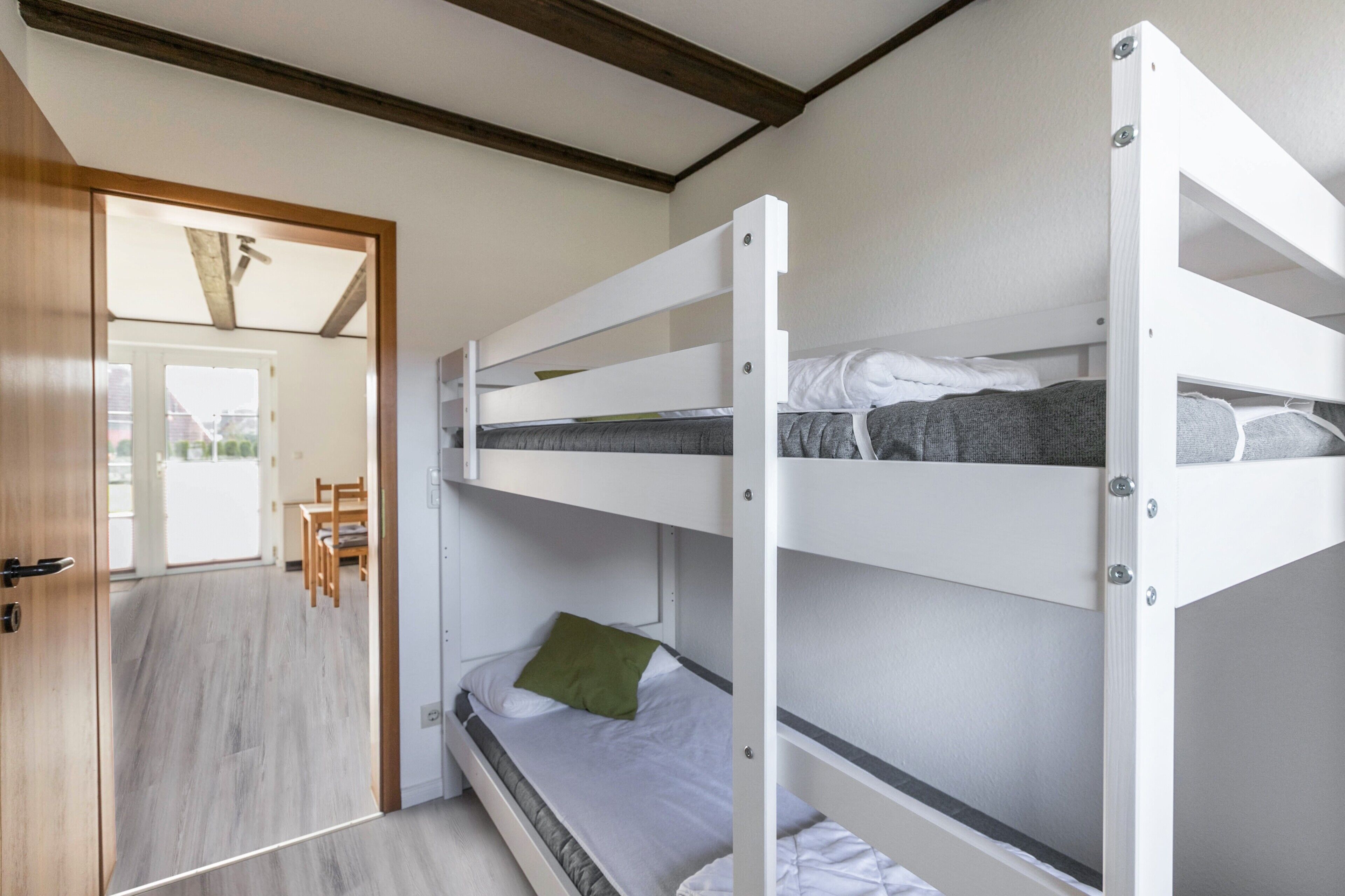 A bunk bed room with a wooden door, a dining area with chairs, and a view of the outside.