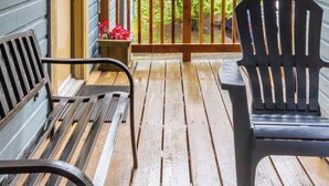 A wooden deck with a railing, two chairs, and a bench.