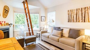 A living room with a sofa, a wooden ladder, a fireplace, and a large window.