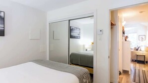A bedroom with a bed, a sliding door closet, a small table, and a view into a living area.
