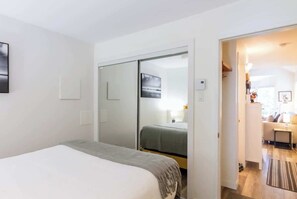 Un dormitorio con cama, armario corredero, una mesita y vistas a un salón.