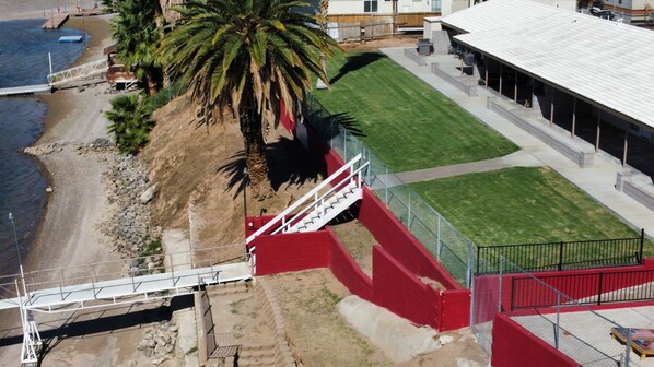 A coastal area with a beach, a palm tree, a staircase, and a building with a covered area.