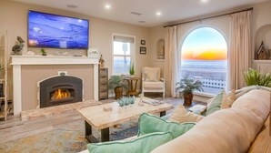 A living room with a fireplace, a television, a sofa, and a view of the sunset through a large window. - 55' Ocean Front * Exclusive Ground Level Patio * A/C (San Diego)