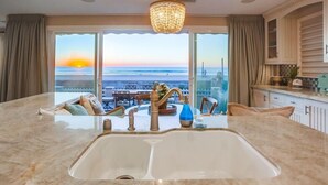 A modern kitchen with a large island, a chandelier, and a view of the ocean at sunset. - 55' Ocean Front * Exclusive Ground Level Patio * A/C (San Diego)